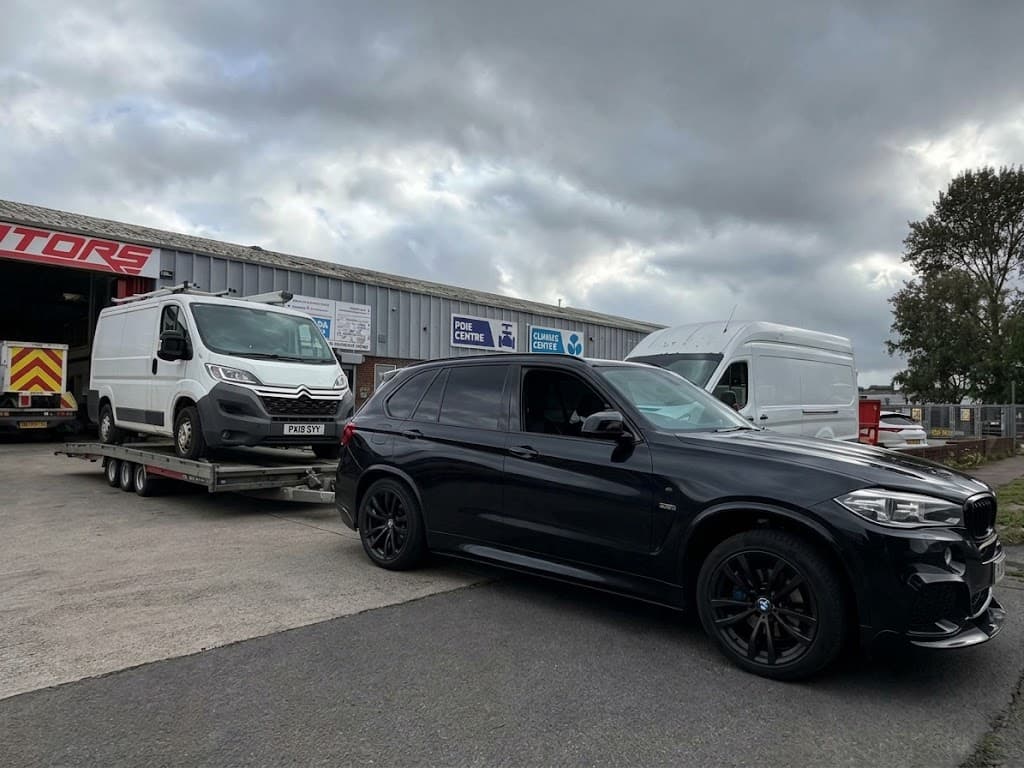 A BMW X5 towing a white Citroen van outside a unit