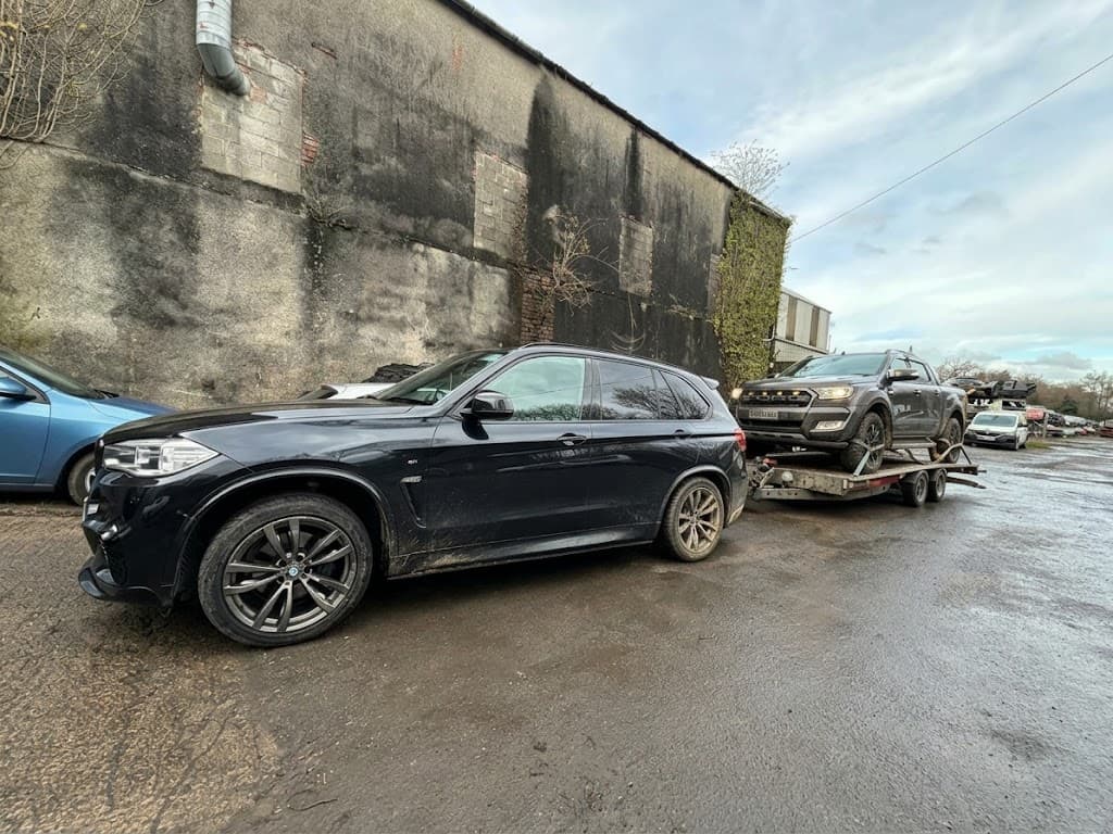 A BMW X5 towing a Ford Ranger pickup on a trailer